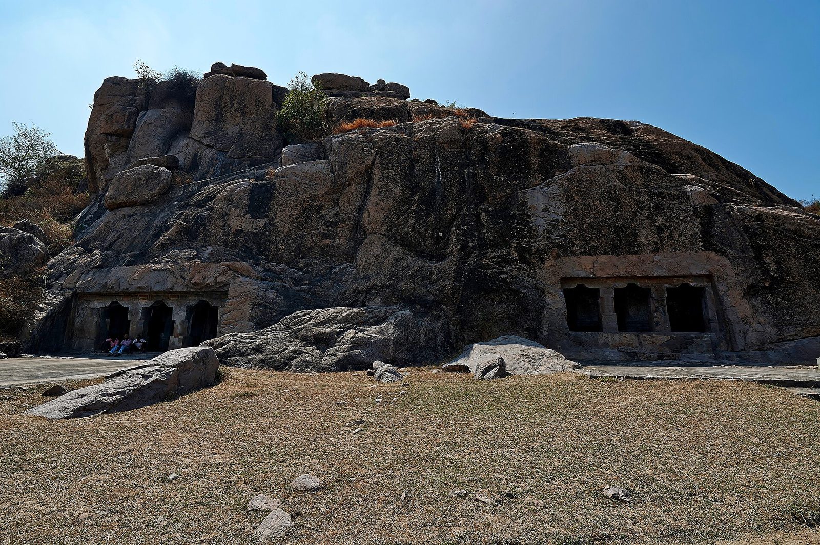Rock-cut cave fronts low in a granite outcrop above a dry field.
