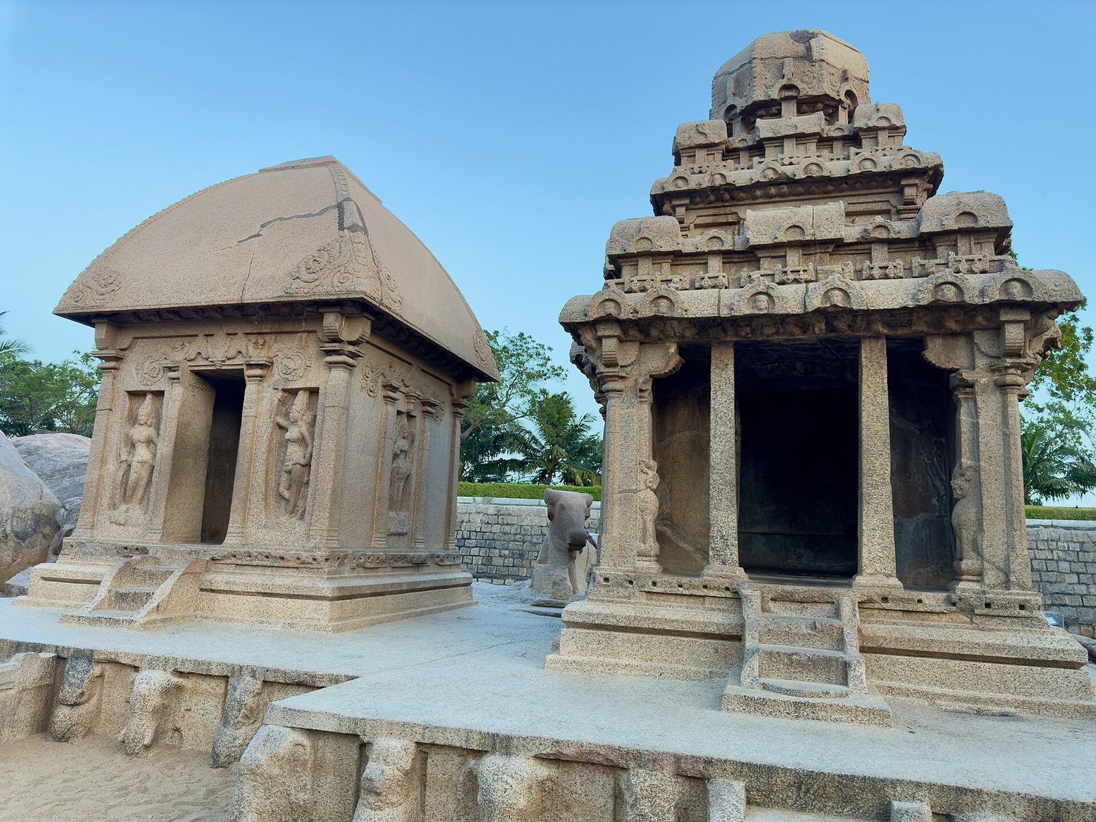 Two monolithic shrines carved from single boulders, one with a thatched-hut roof and one with a stepped tower.