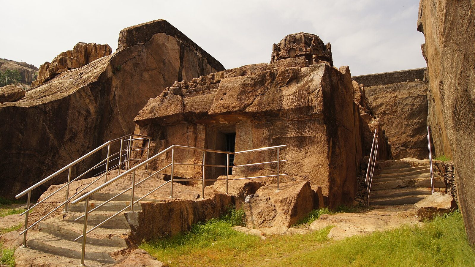 An unfinished temple carved down into a rock hill, with steps and railings around it.