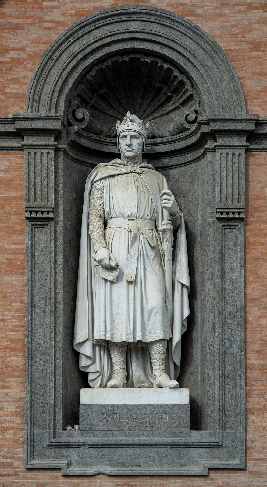 A white marble statue of a crowned king in a long robe holding a sceptre, standing in a round-headed niche in a palace front.
