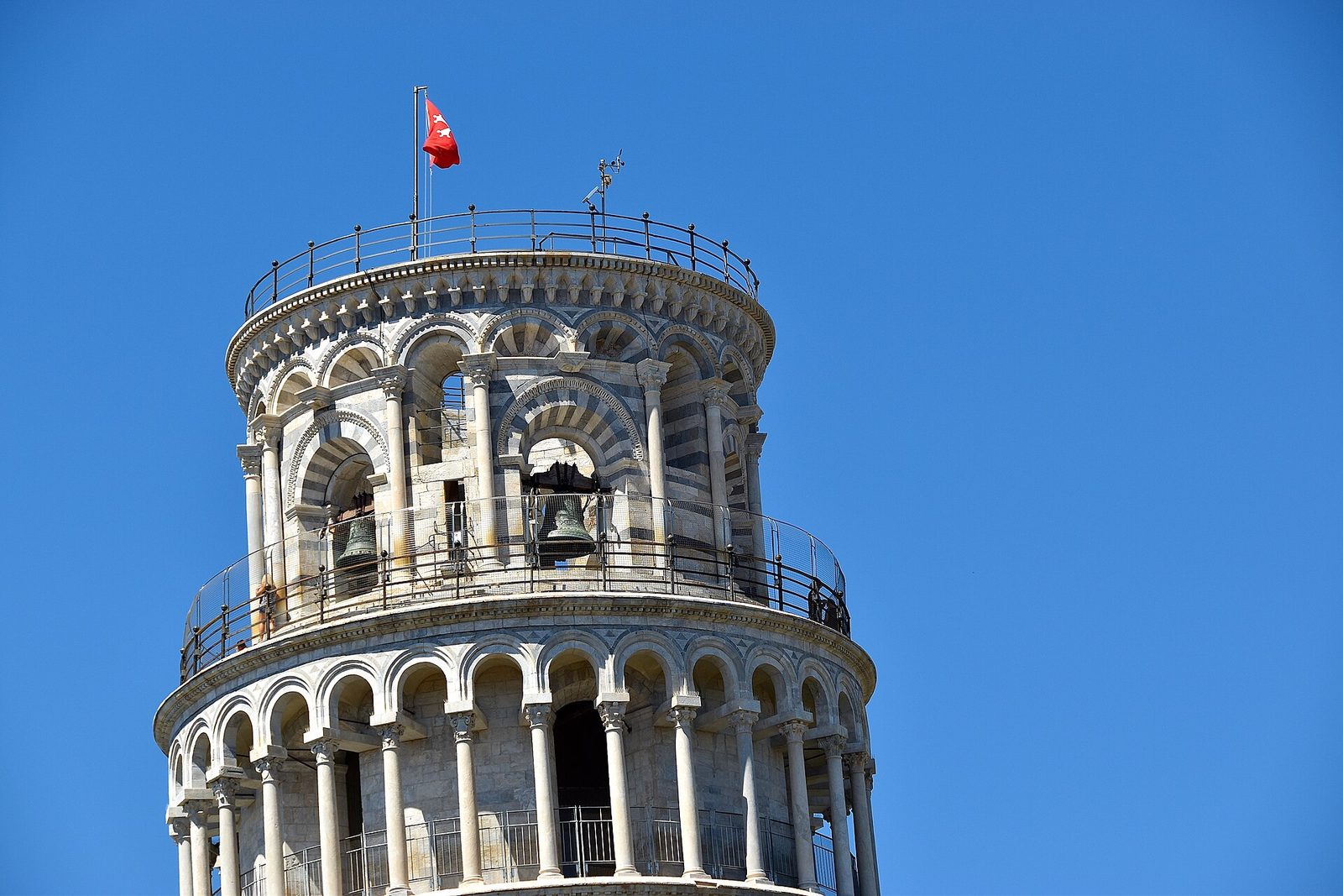 A round marble bell tower of stacked open arcades leaning visibly out of true, with the end of a cathedral beside it.