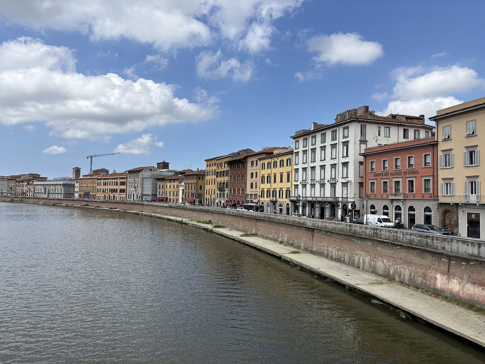 A river running between stone embankments with rows of tall pastel houses along both banks and a church dome rising among them.