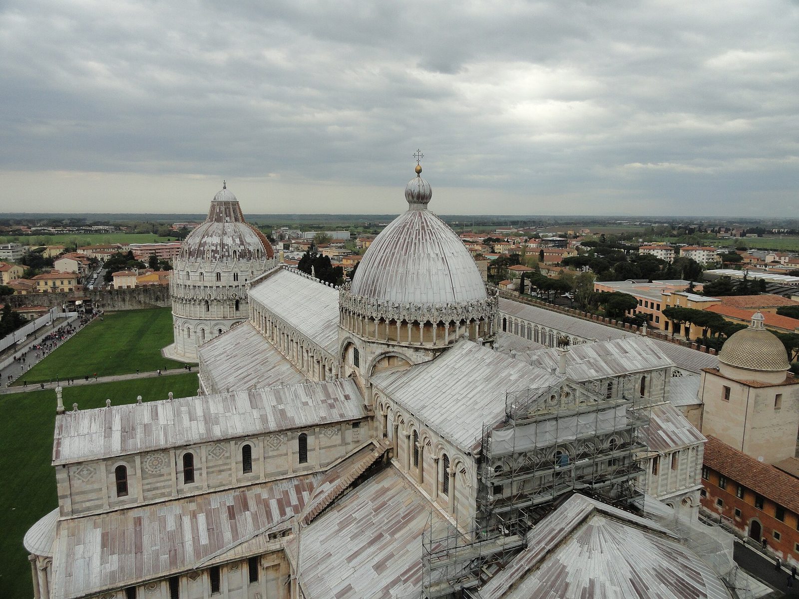 A round domed baptistery of white marble with tiers of arcading and gabled niches, standing on mown grass beside the flank of a cathedral.