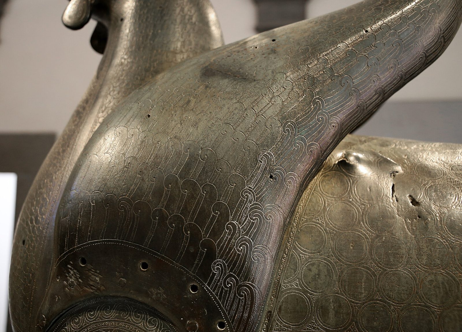 A large bronze griffin standing stiffly with folded wings, its body incised all over with feather patterns and a band of Arabic lettering round the chest.