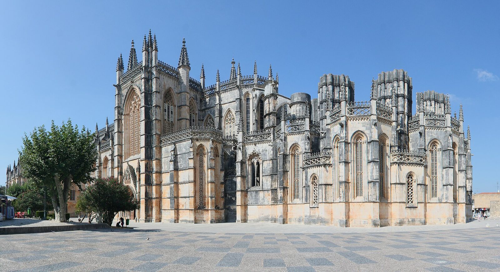 A great Gothic church of honey-coloured stone with pinnacles and flying buttresses, seen across a paved square.