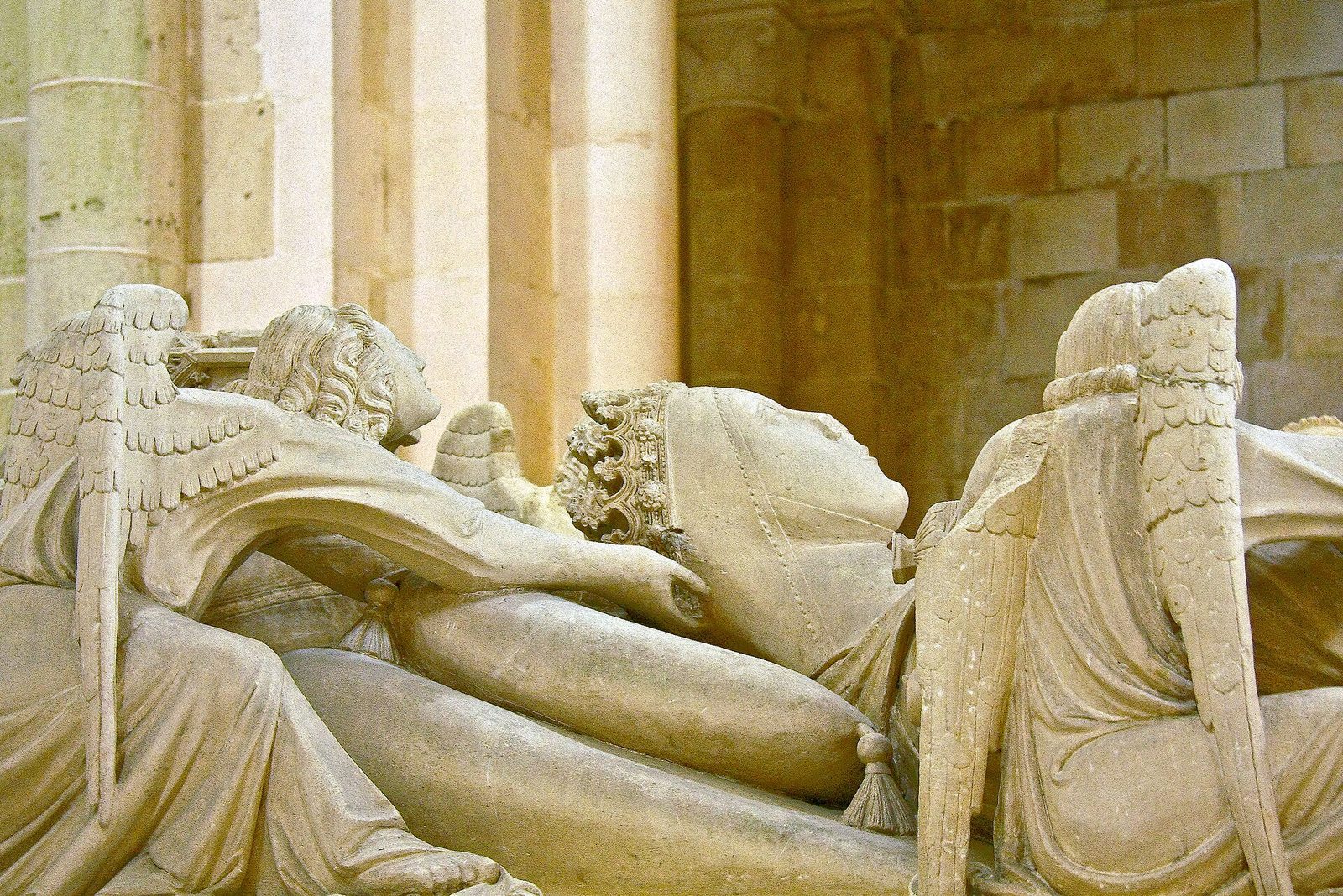 A carved stone tomb with a recumbent crowned woman, angels at her head, under a Gothic arch.