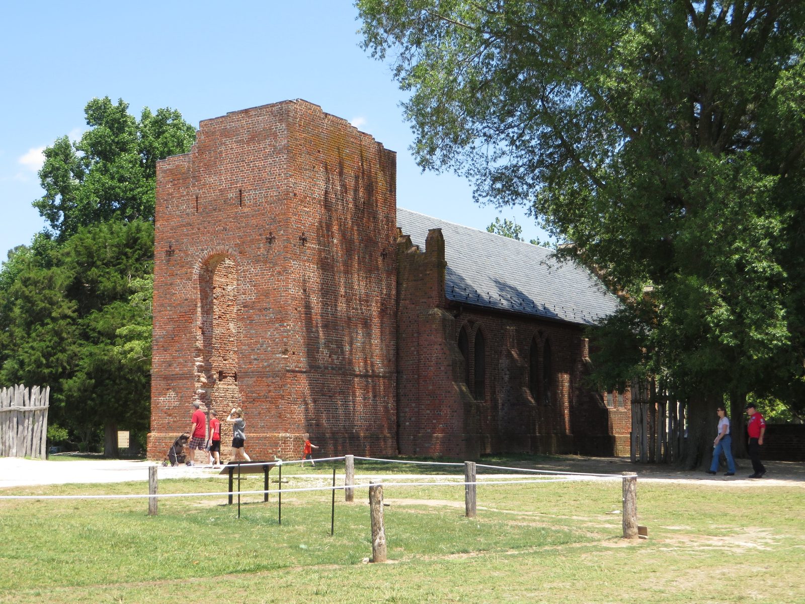 A ruined brick church tower beside a later brick church, with visitors on the lawn.