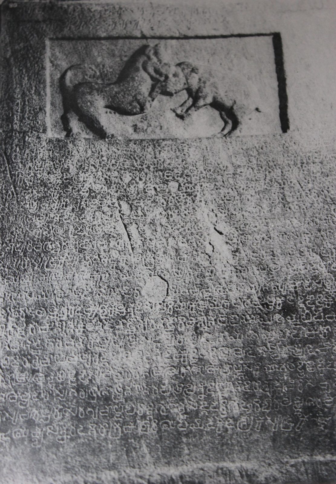 A stone slab with a relief of a hound fighting a boar above lines of old Kannada.