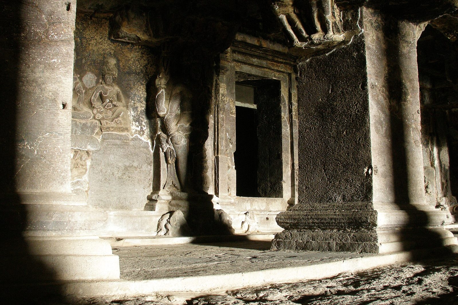 A dim rock-cut hall with carved pillars and a shrine doorway.