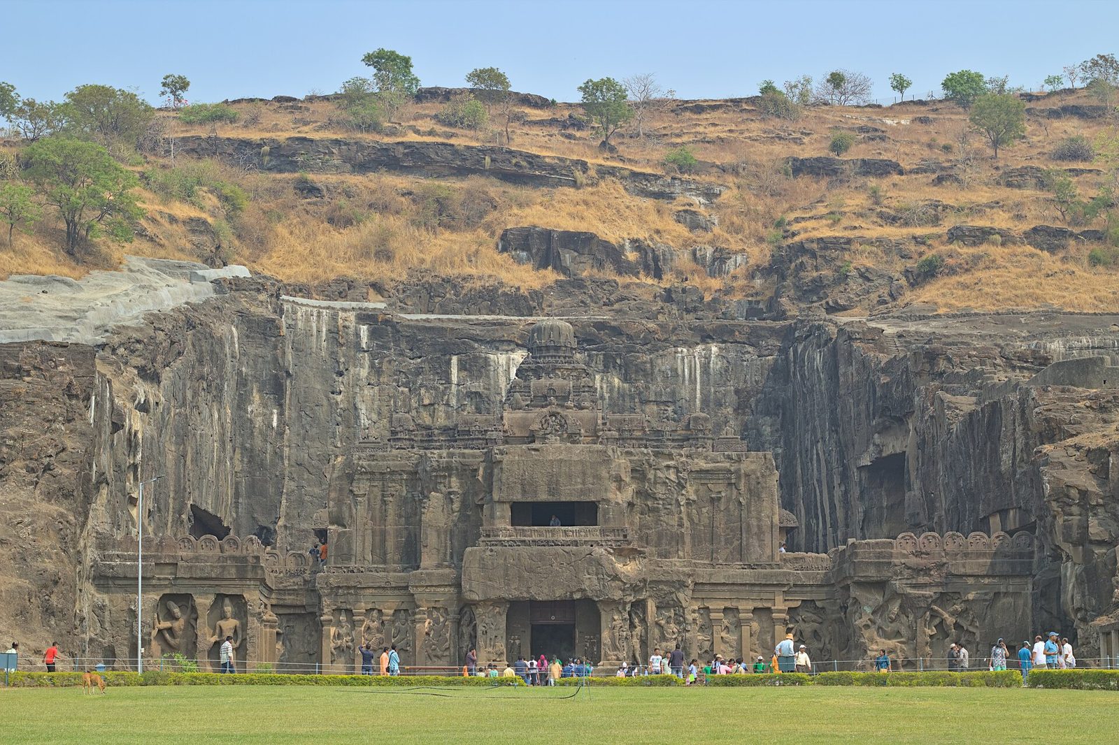 A huge rock-cut temple carved out of a cliff face, seen across a lawn.