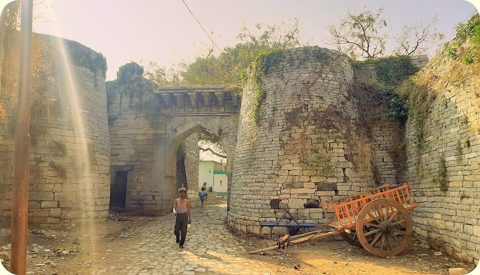 A ruined stone gateway in thick fort walls, with a cart outside.