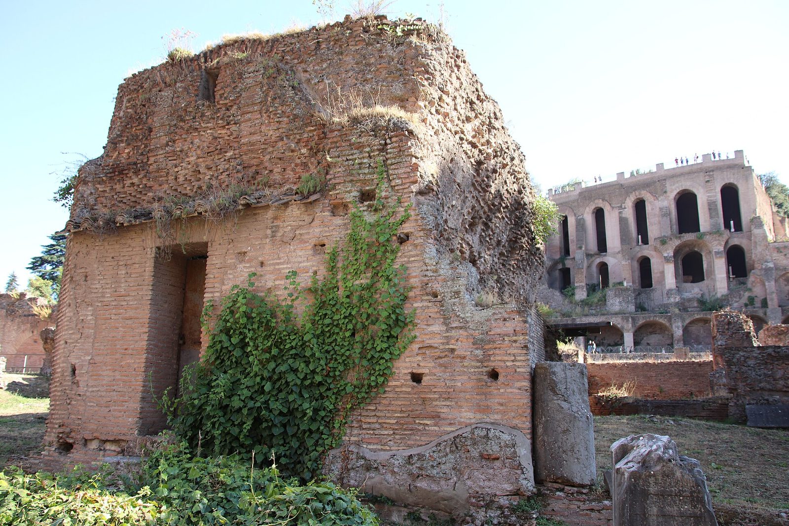 A long rectangular court open to the sky, lined with the stumps of columns and with headless and weathered marble statues standing along one side, brick walls rising behind.
