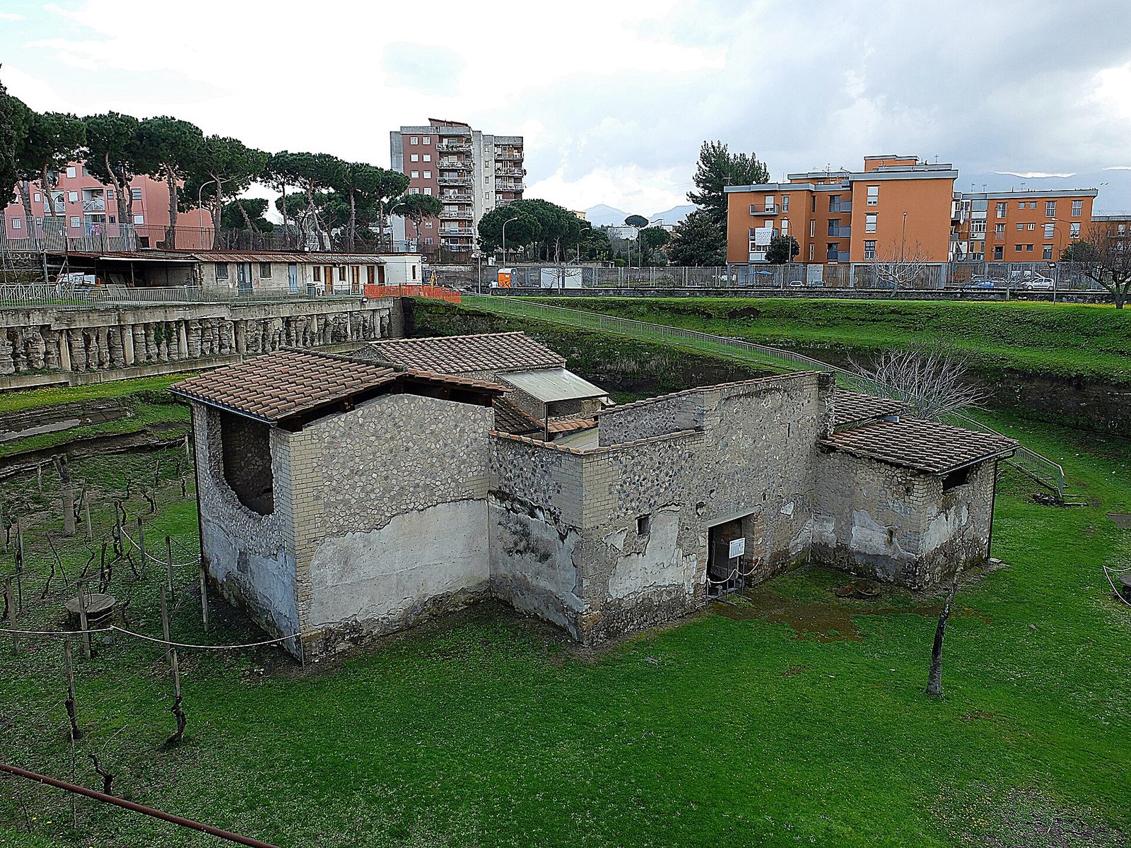 An excavated farm courtyard with the mouths of huge buried storage jars set flush into the paving in rows, low walls and a portico around them.