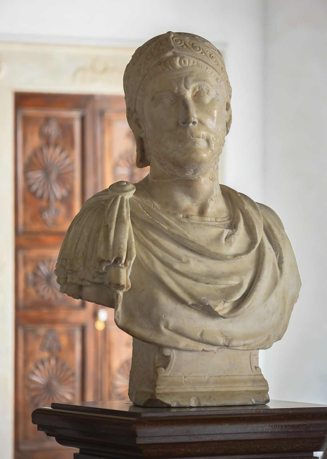 A marble head of a young man with short curling hair and a slightly turned face, the nose and surface worn, displayed against a plain background.
