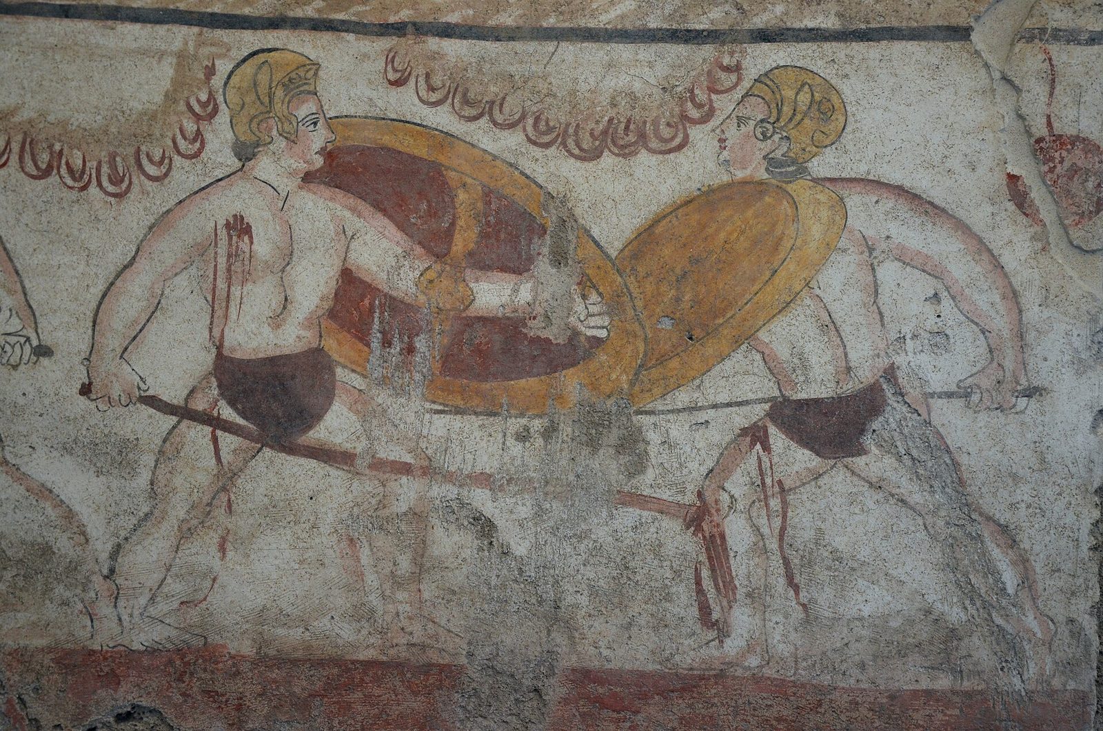 A painted tomb slab showing two warriors facing each other with round shields, crested helmets and levelled spears, their flesh reddish and the background a pale plaster.