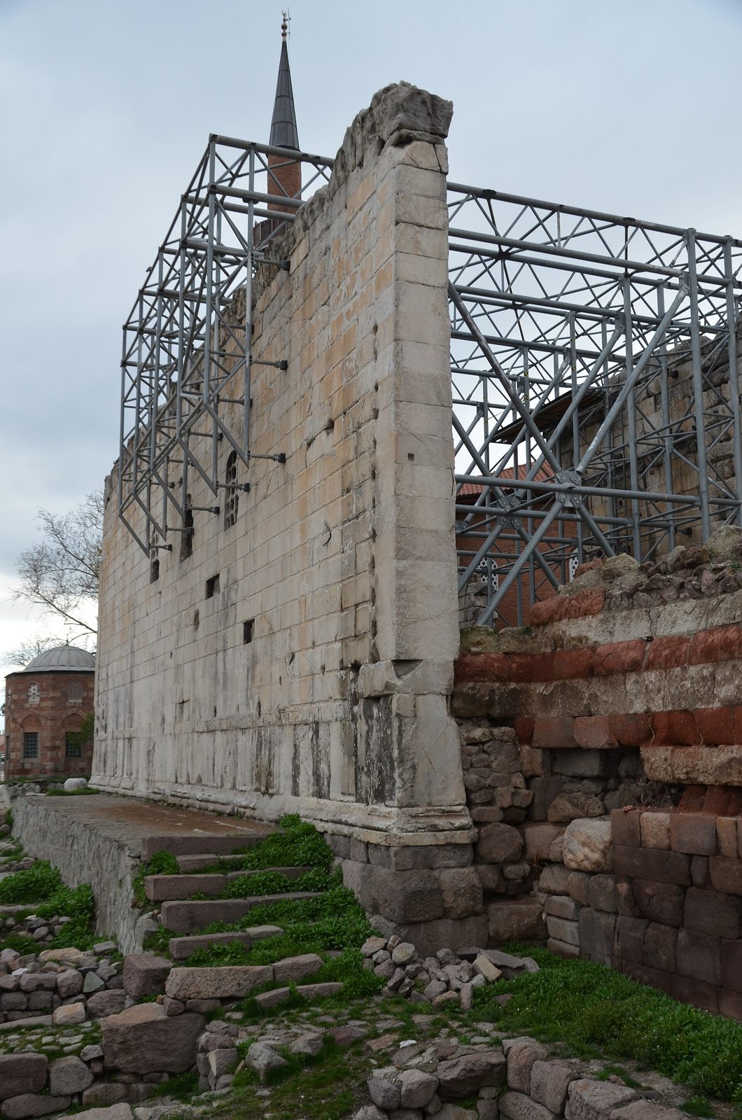 A high wall of weathered marble blocks, its inner face covered from top to bottom with closely cut columns of Latin, a doorway with a carved frame at one end.