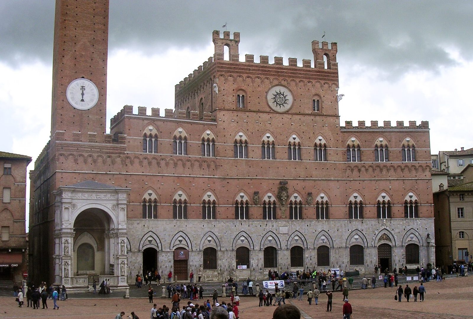 A brick civic palace with a slightly concave front, rows of pointed three-light windows and a crenellated roofline, a tall tower rising at one side.