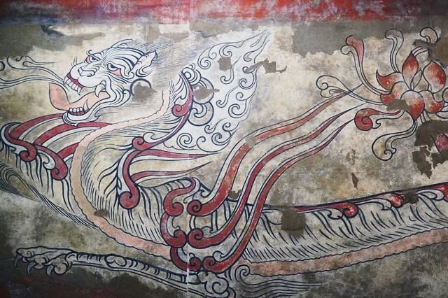 A wall painting of a fantastic beast with a curling crest and red and black swirling body.