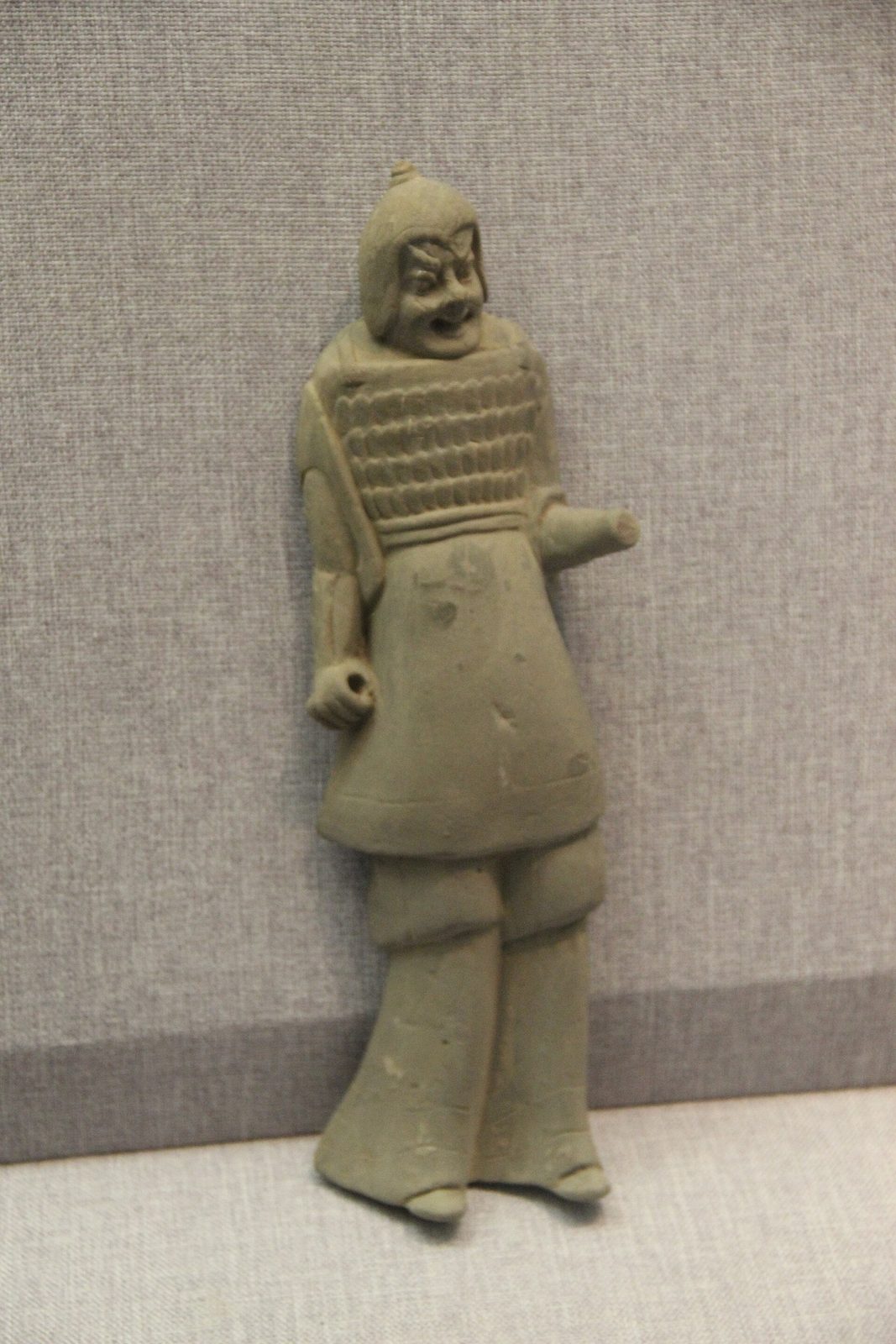 A pottery figure of a standing soldier in a hood and scaled armour.