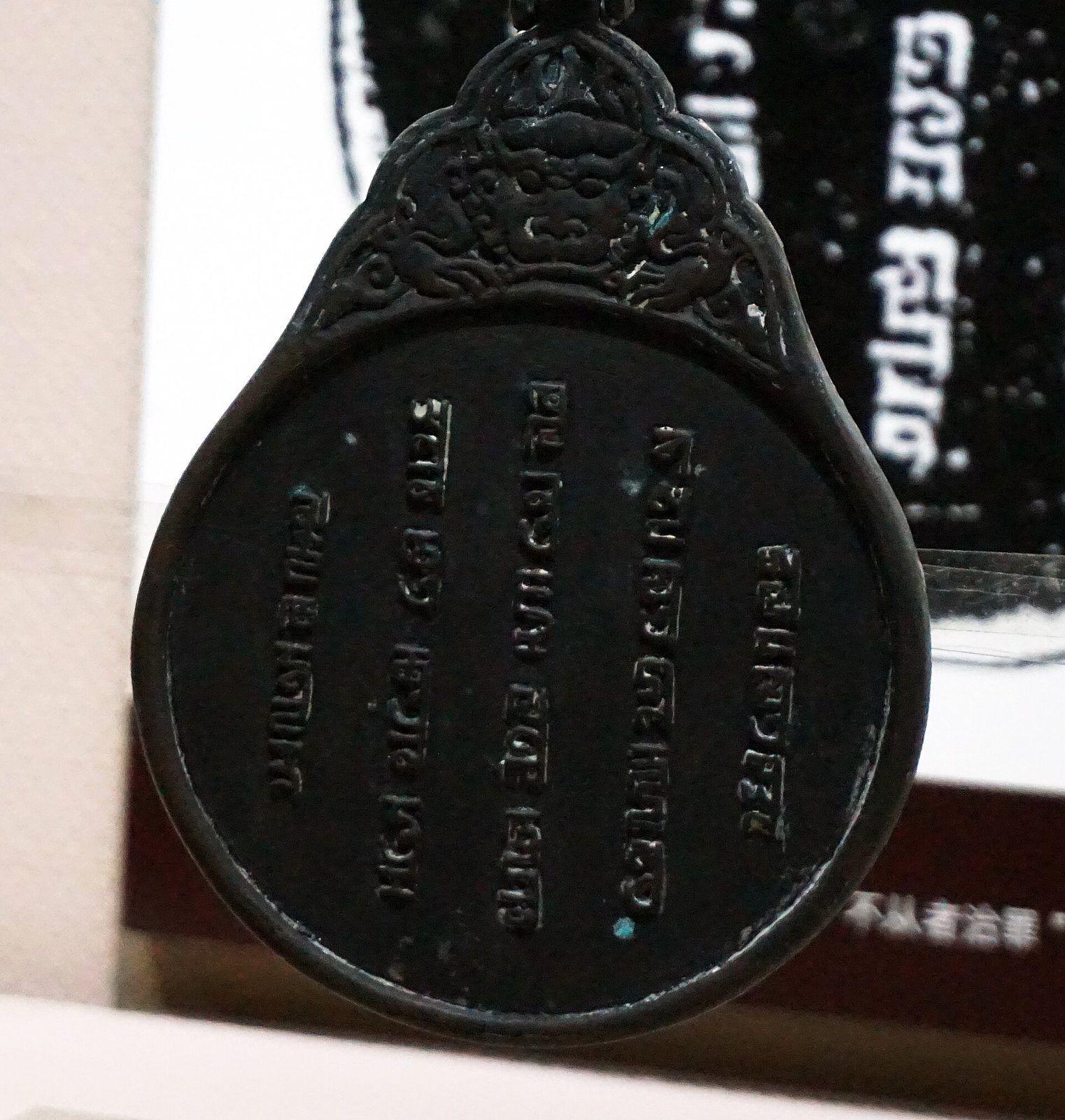 A dark round tablet with a decorated top, its face carved with columns of square Phags-pa letters.