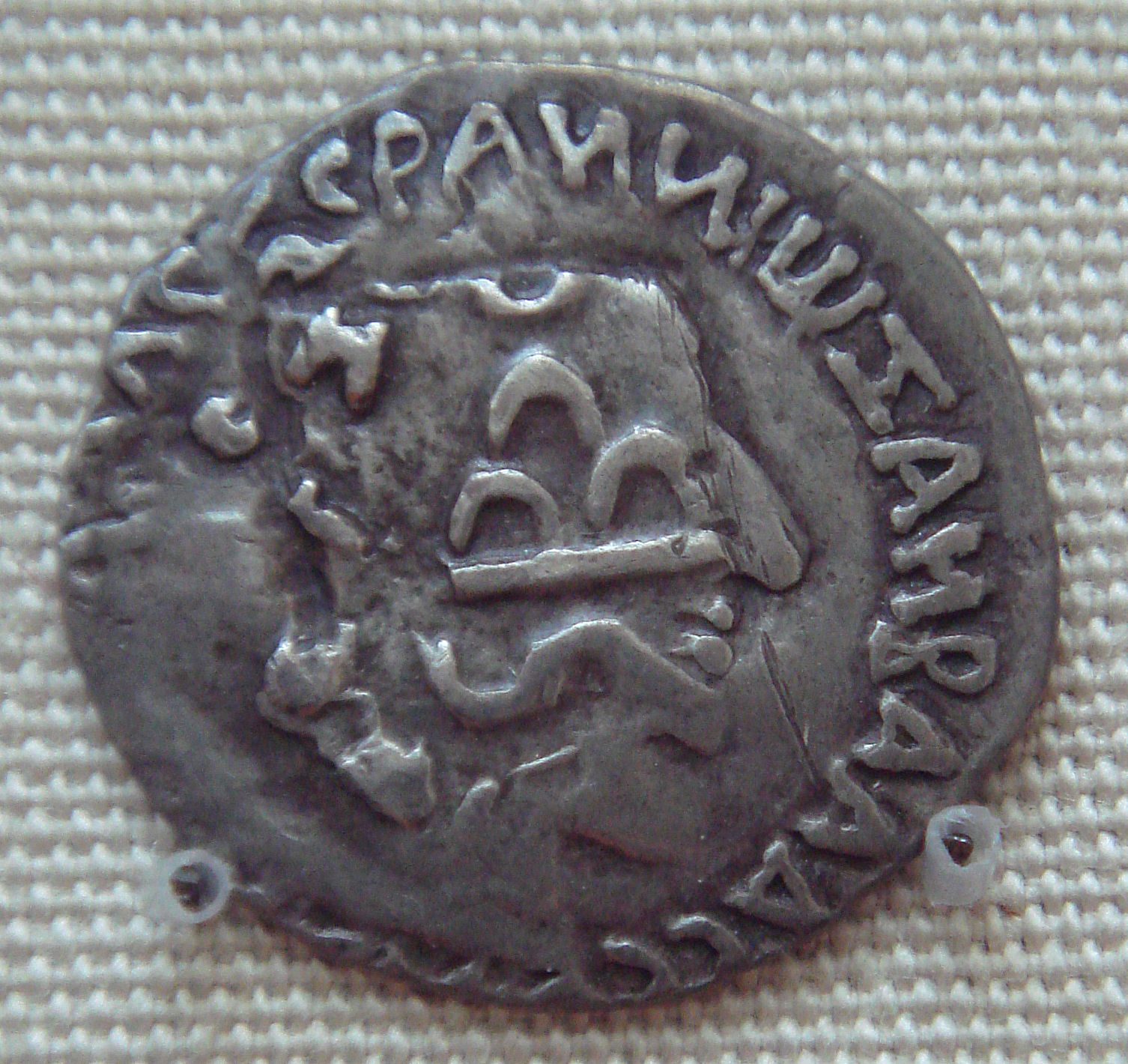 A worn silver coin with the profile of Nahapana and a Greek legend, overstamped with other symbols.
