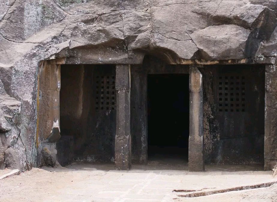A plain rock-cut cave front with a doorway and two latticed windows.