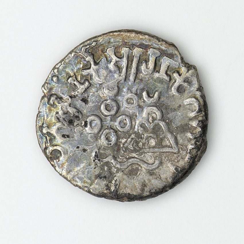 A silver coin with a Brahmi legend around a hill symbol.