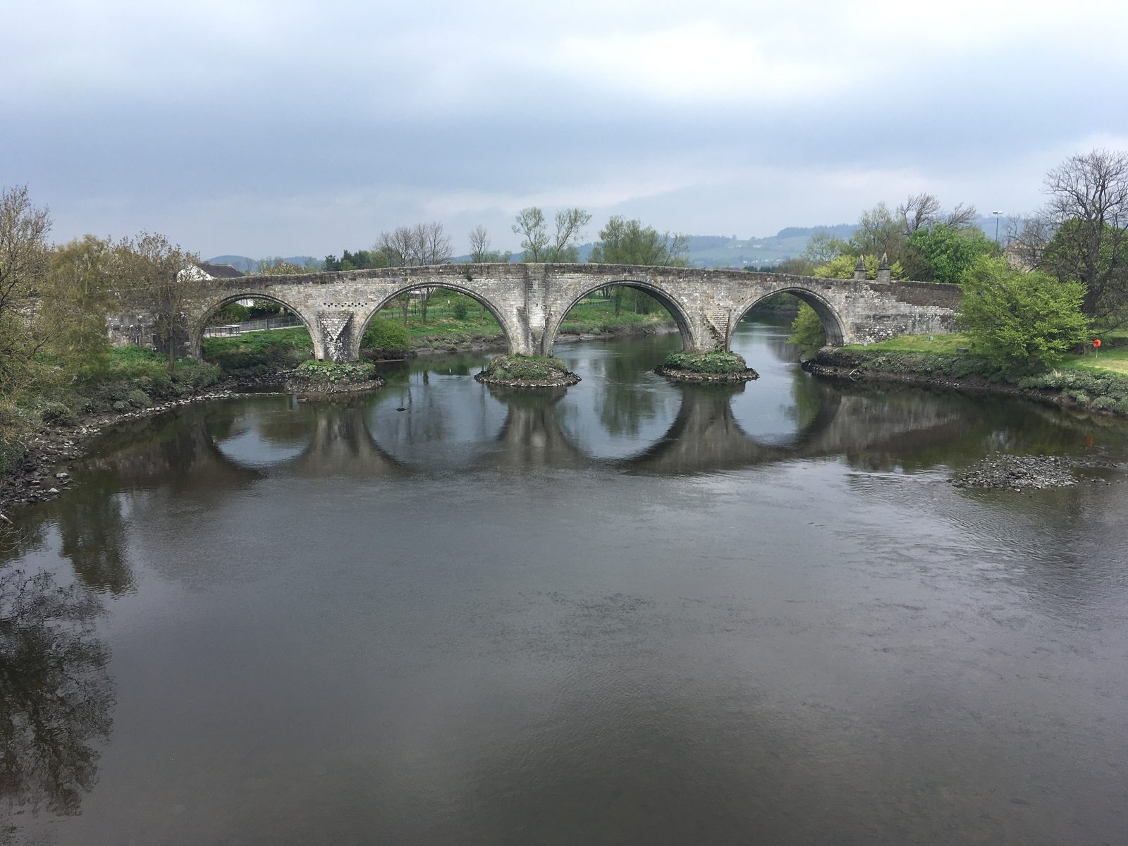 A four-arched stone bridge reflected in a still river.