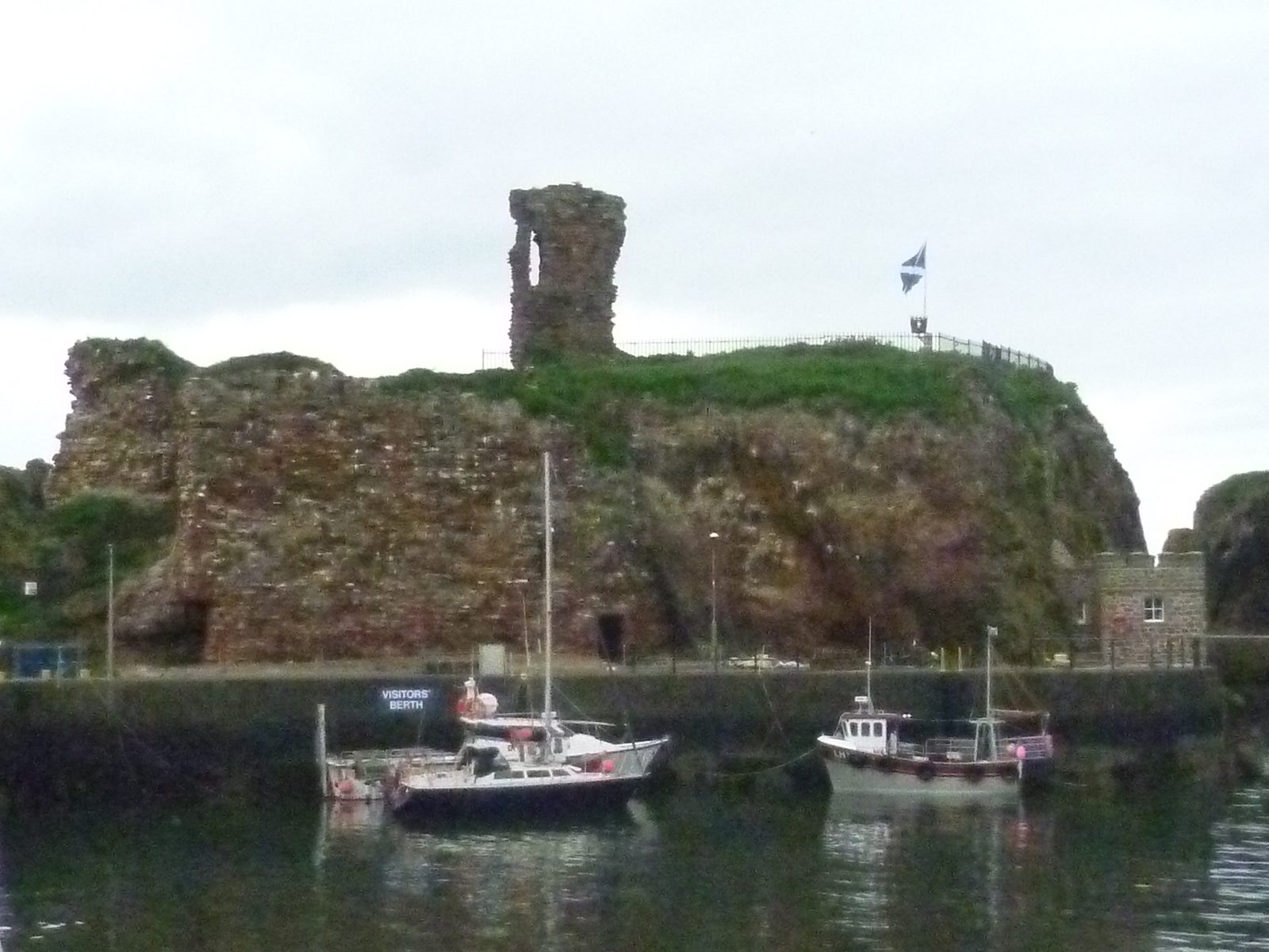 Red sandstone ruins on a rock above a harbour with small boats.