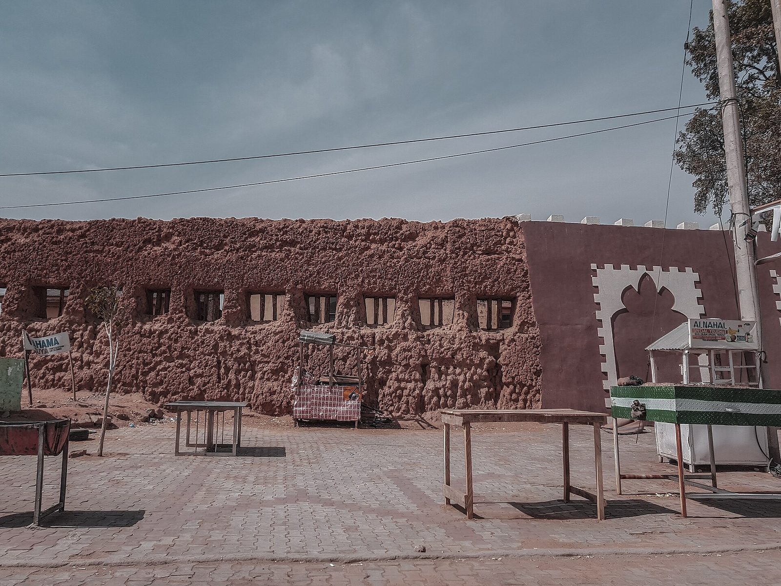 A stretch of thick weathered earthen wall beside a paved square with market tables.
