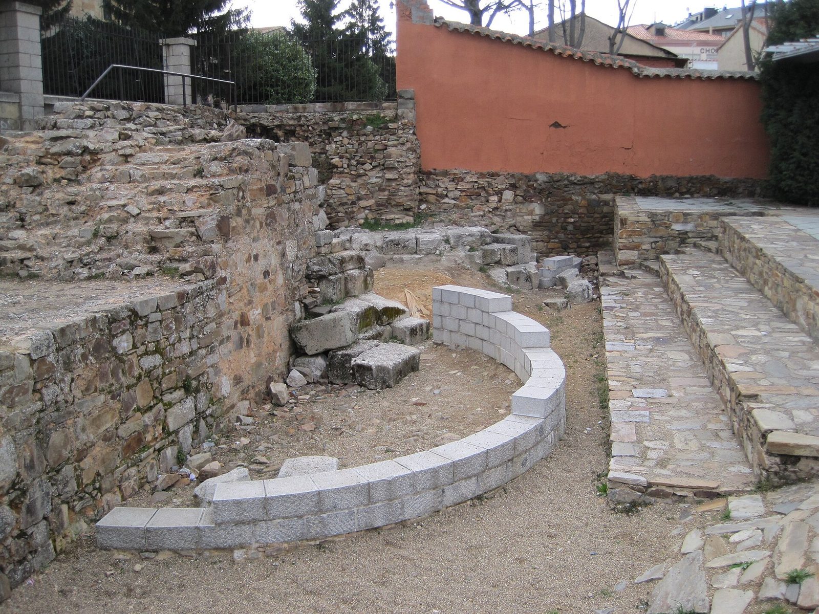 A massive Roman wall of rough masonry curving round a projecting semicircular tower, with grass at its foot and a town roofline behind.