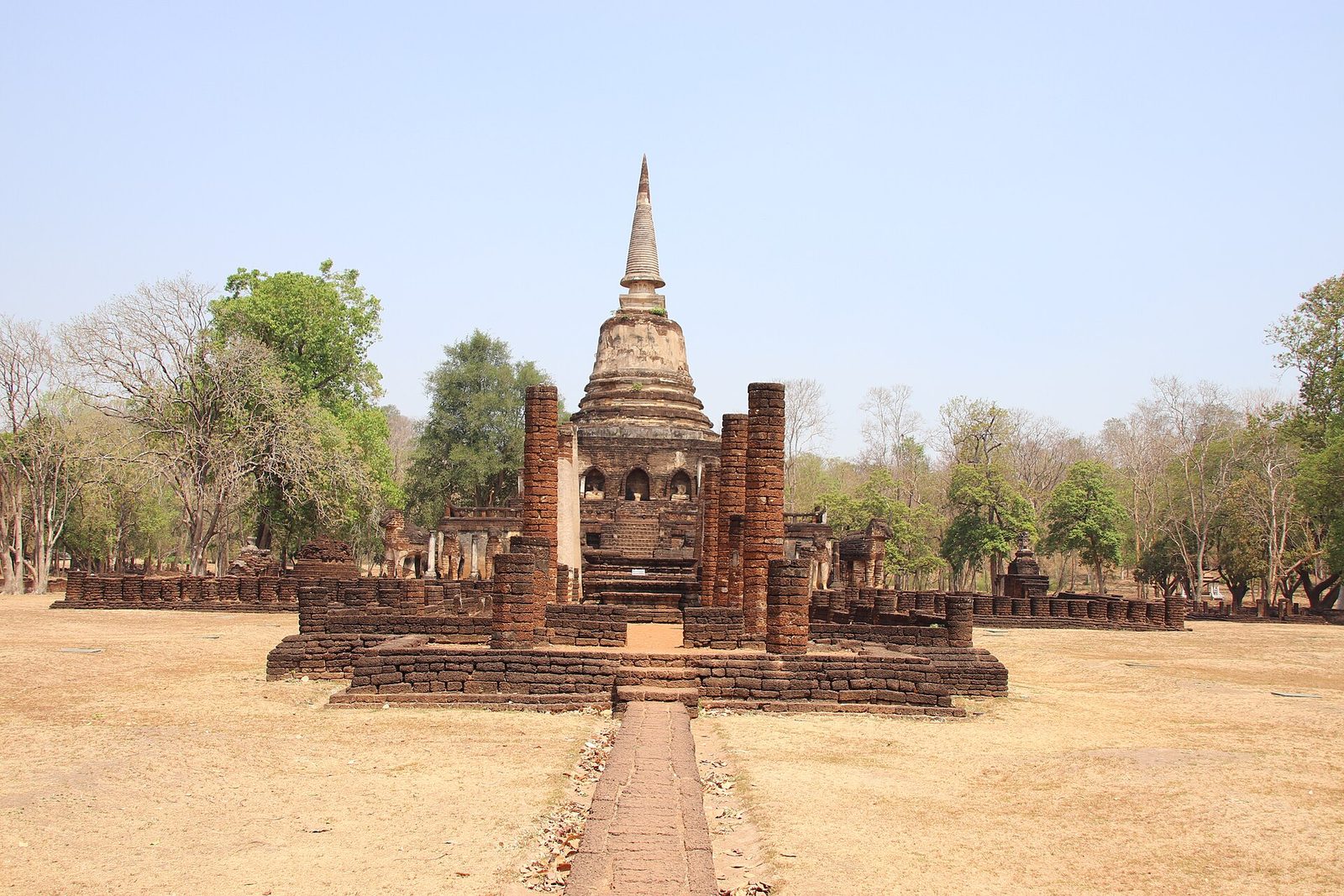 A ruined bell-shaped stupa on a terrace at the end of a brick path.