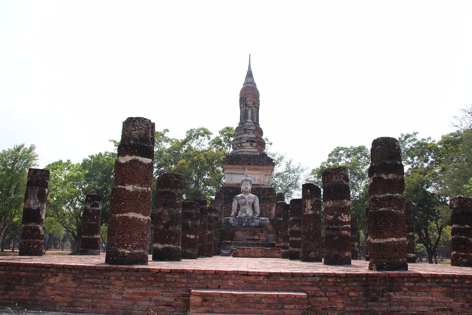 Rows of ruined brick columns before a lotus-bud spire and a seated Buddha.