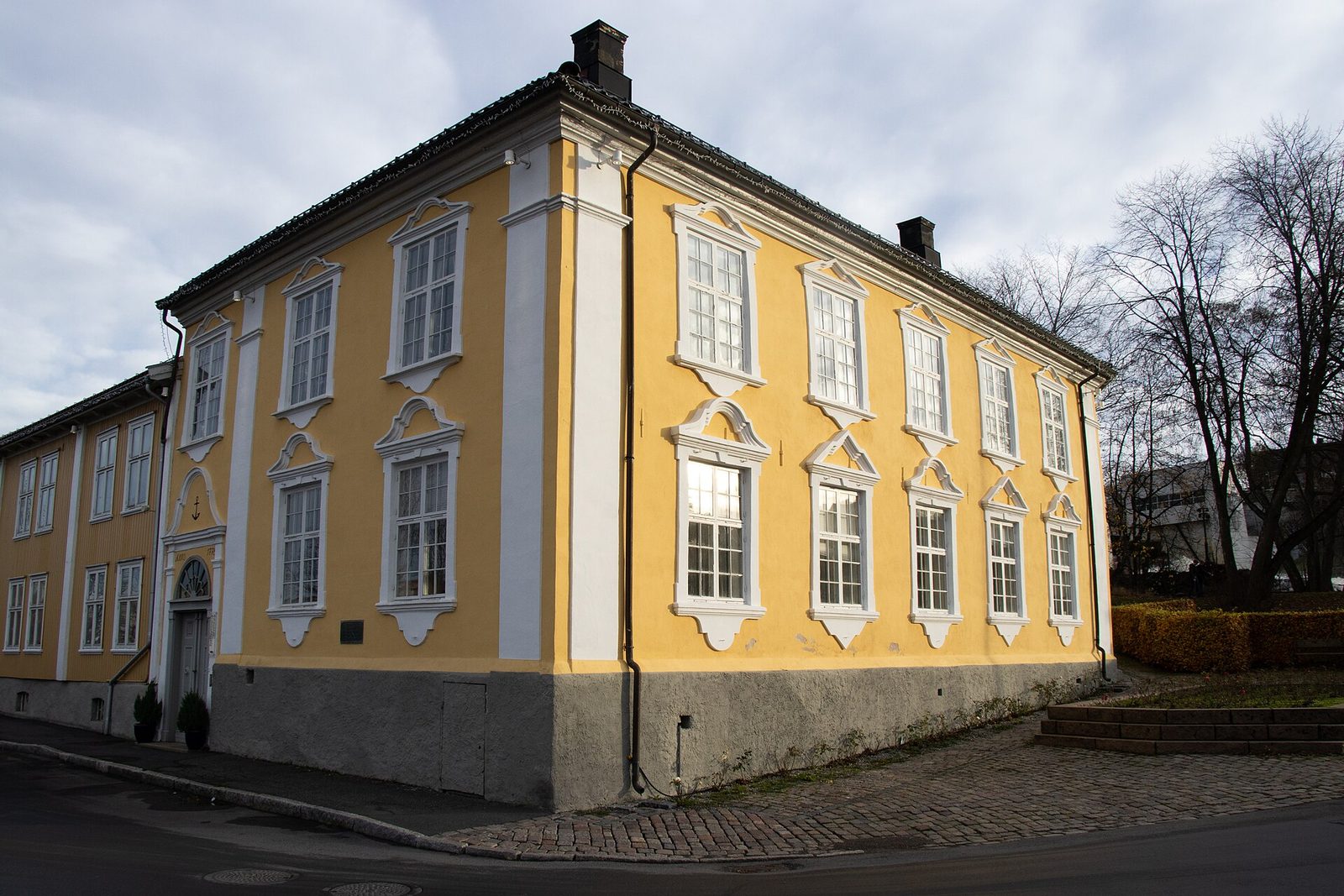 A yellow two-storey wooden house on a street corner, bare trees behind.