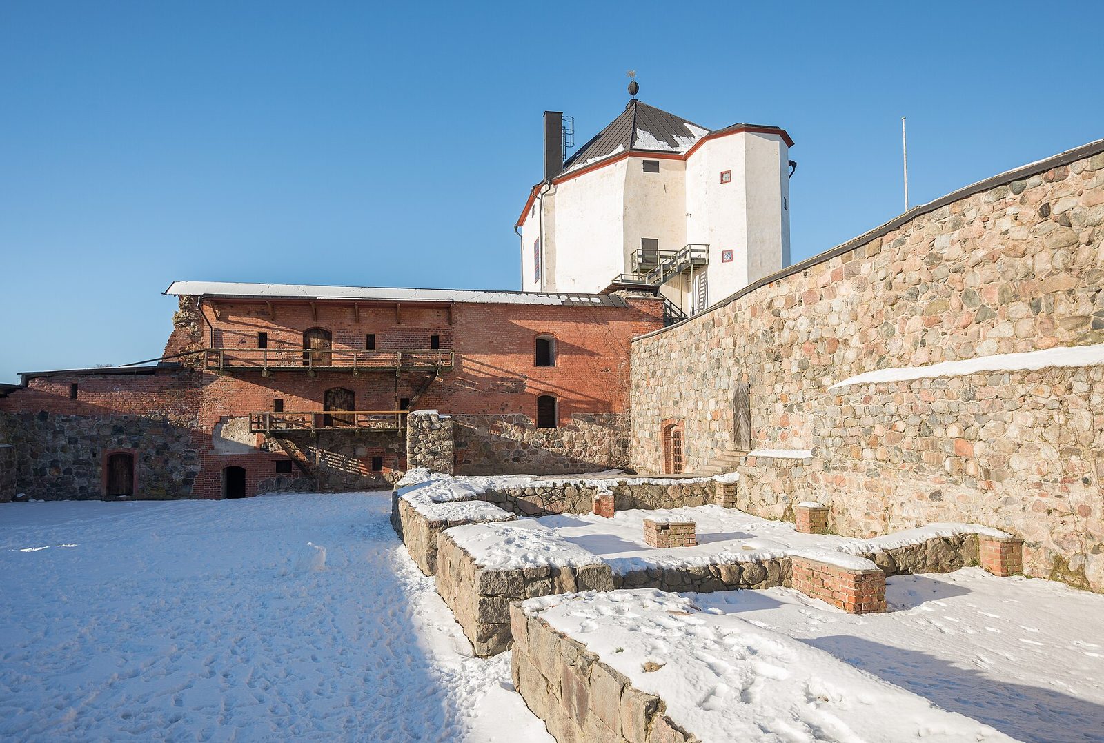The courtyard of a castle in snow, a white keep rising behind stone walls and a red ruined range.
