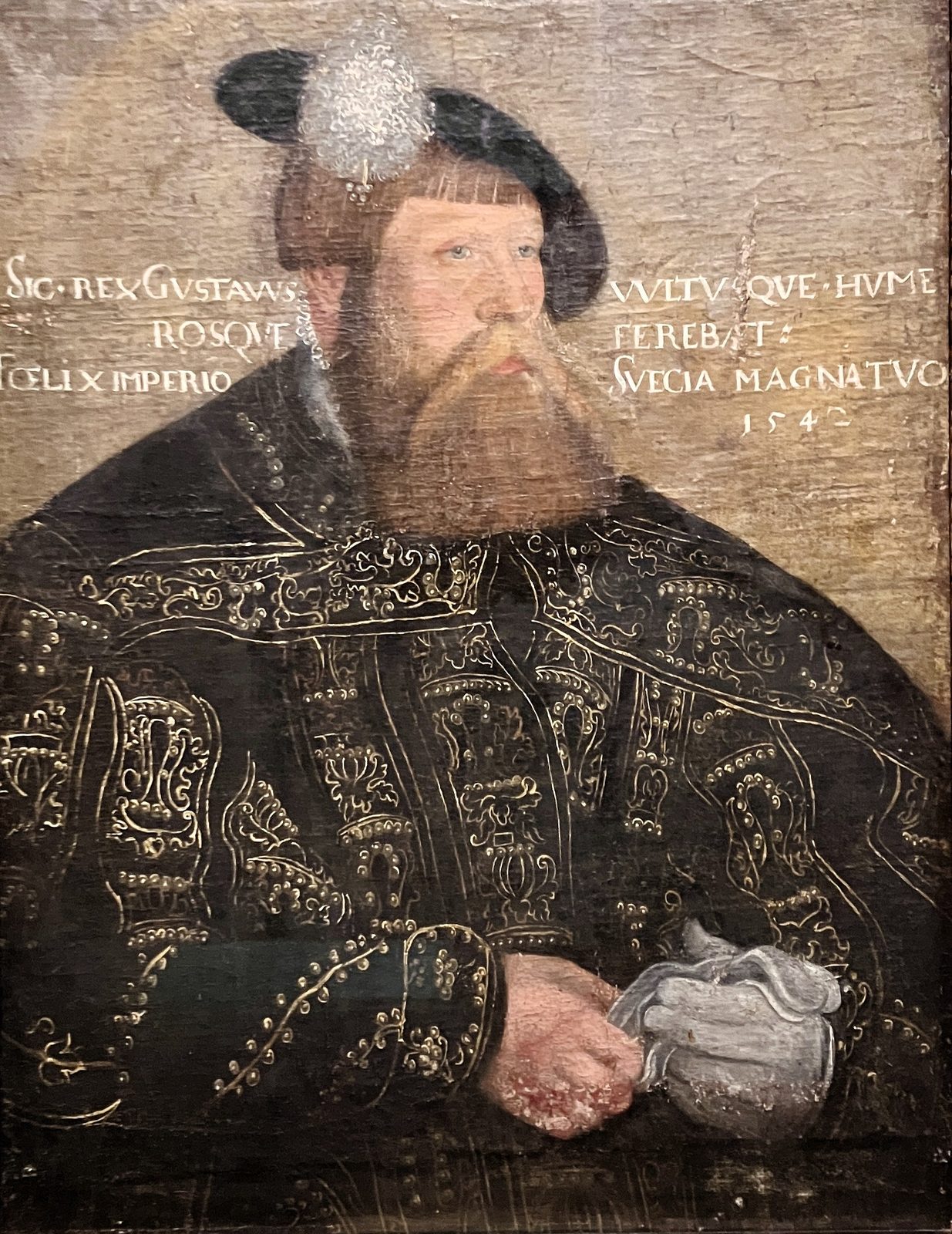 A portrait of a bearded king in a black embroidered coat and a feathered cap, a Latin inscription across the background.