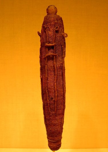 A long cylindrical figure of tightly woven coconut fibre with a rounded head, against an orange background.