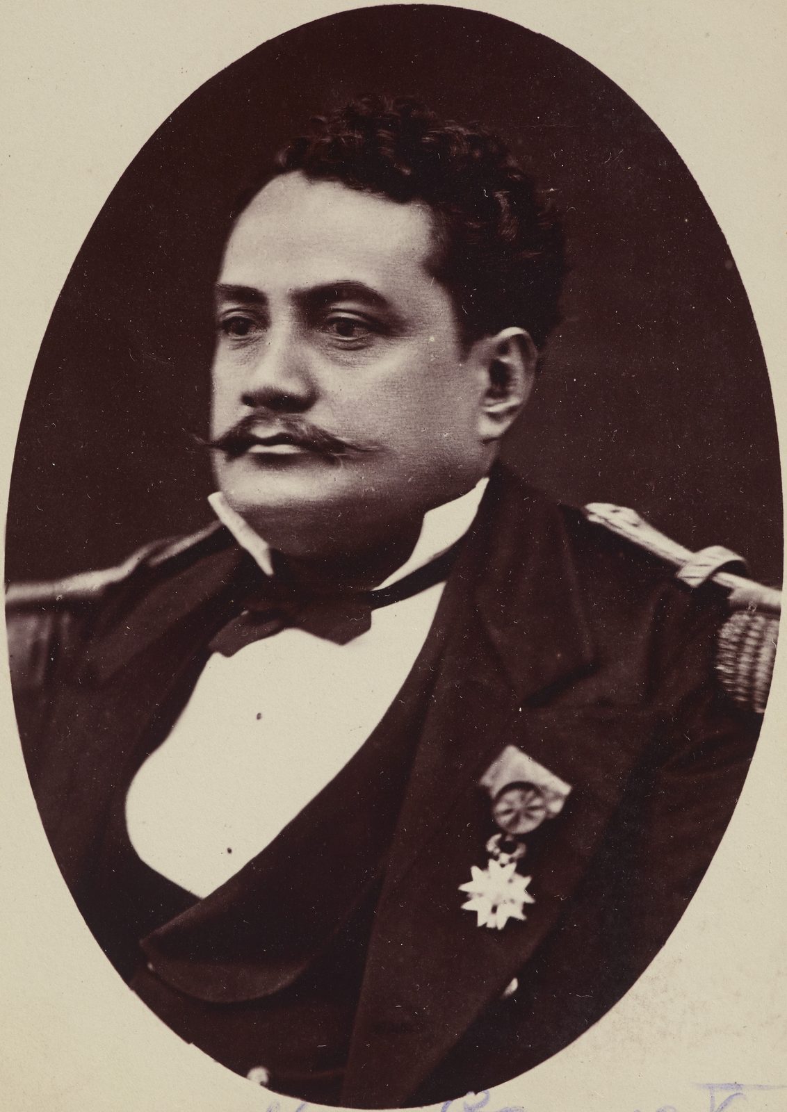 An oval photograph of a heavy-set man with a large moustache in a naval- style uniform with a medal.