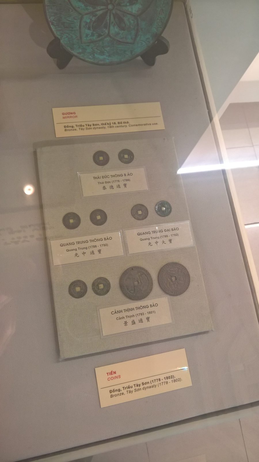 Bronze coins with square holes mounted on a card in a museum case.