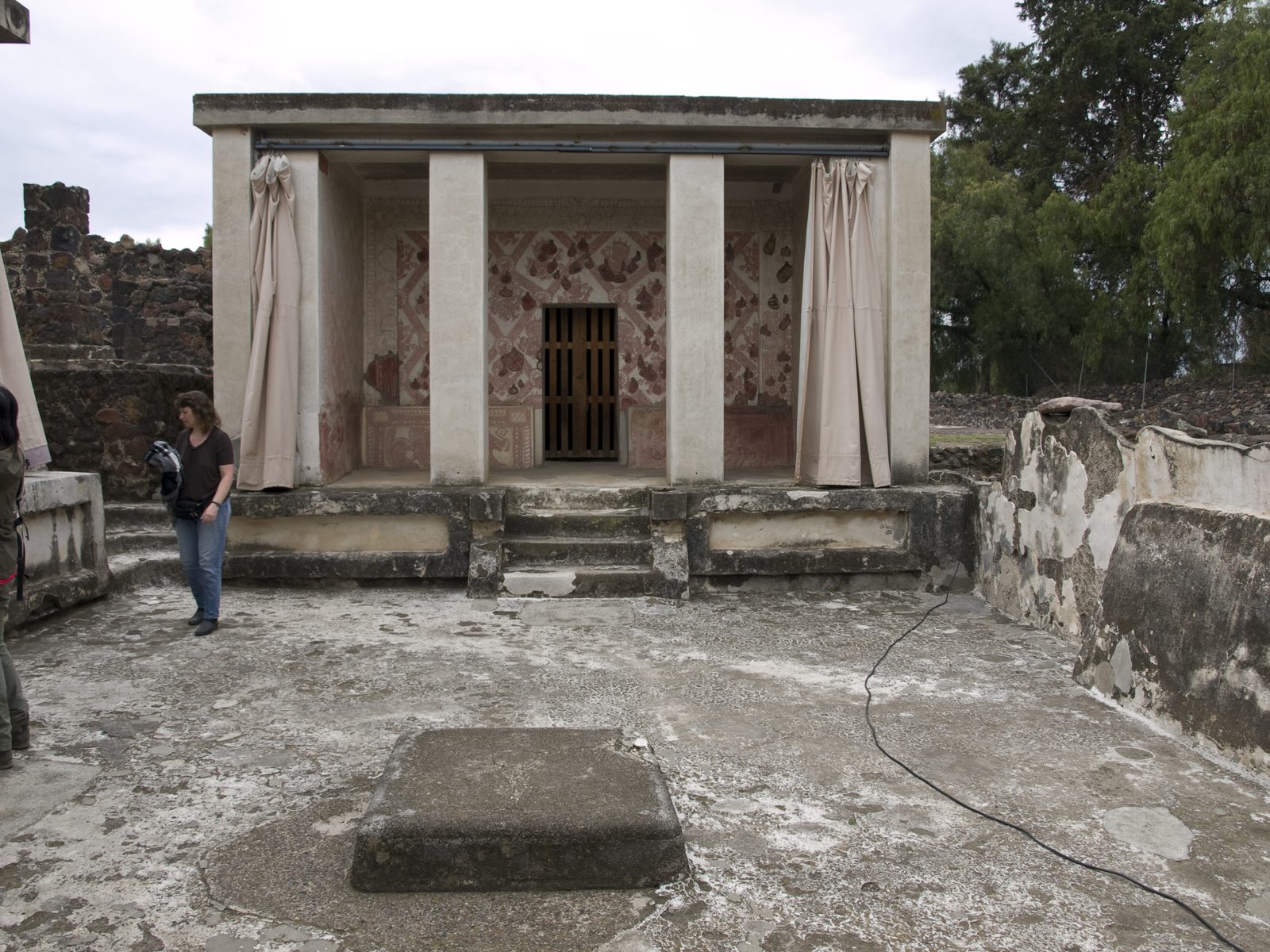 A small courtyard with a pillared portico, painted wall panels and a low central altar.