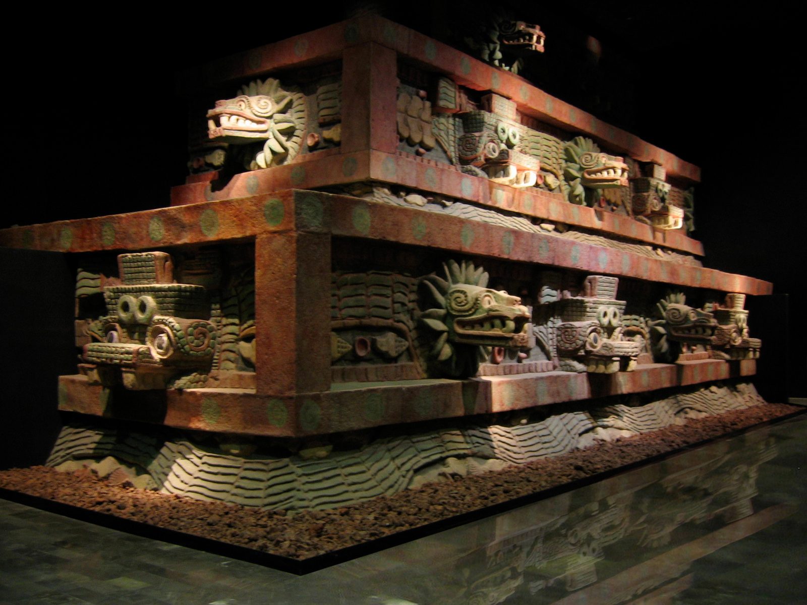 A full-size reconstruction of a stepped temple front with projecting serpent heads, painted red and green, in a dark museum hall.