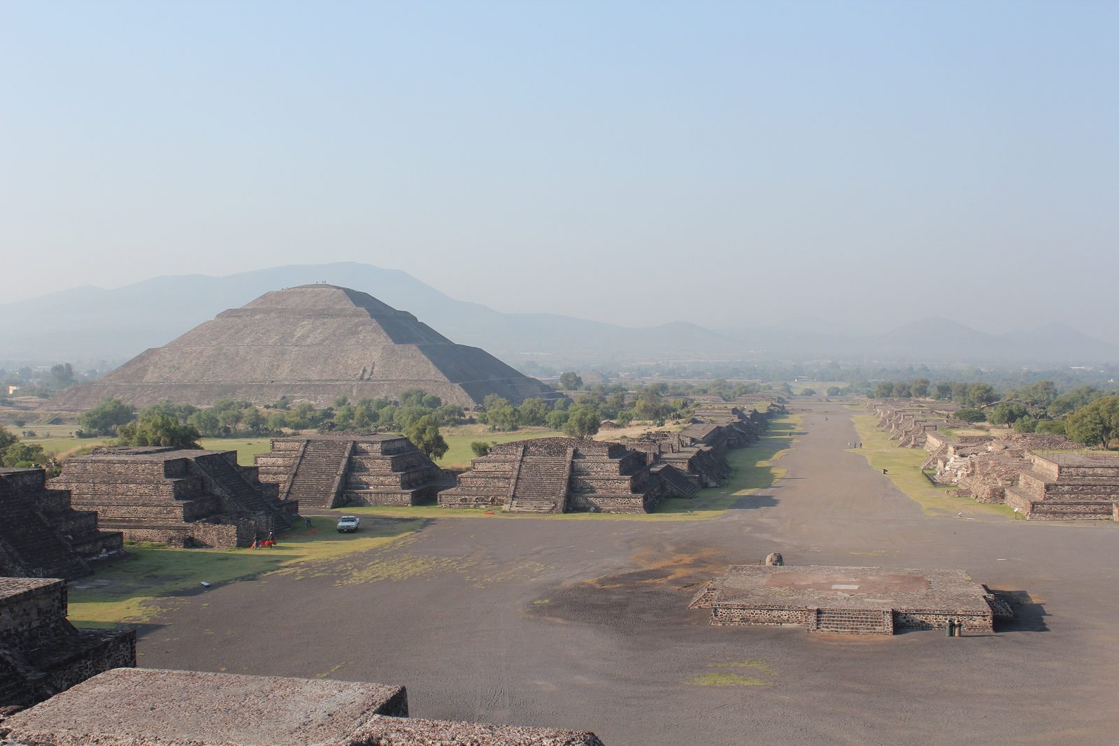A long straight avenue lined with stepped platforms leading toward a huge pyramid, seen from above.