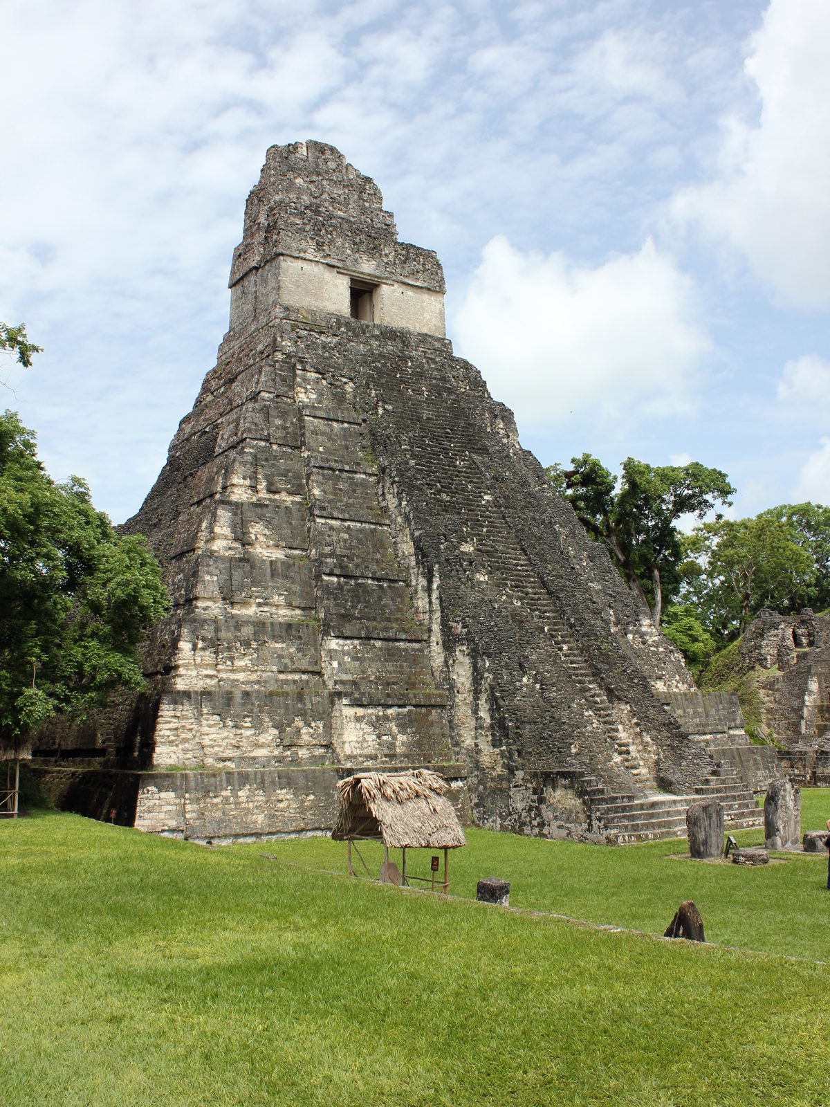 A steep stepped pyramid topped by a temple with a roof comb, rising from a grassy plaza.