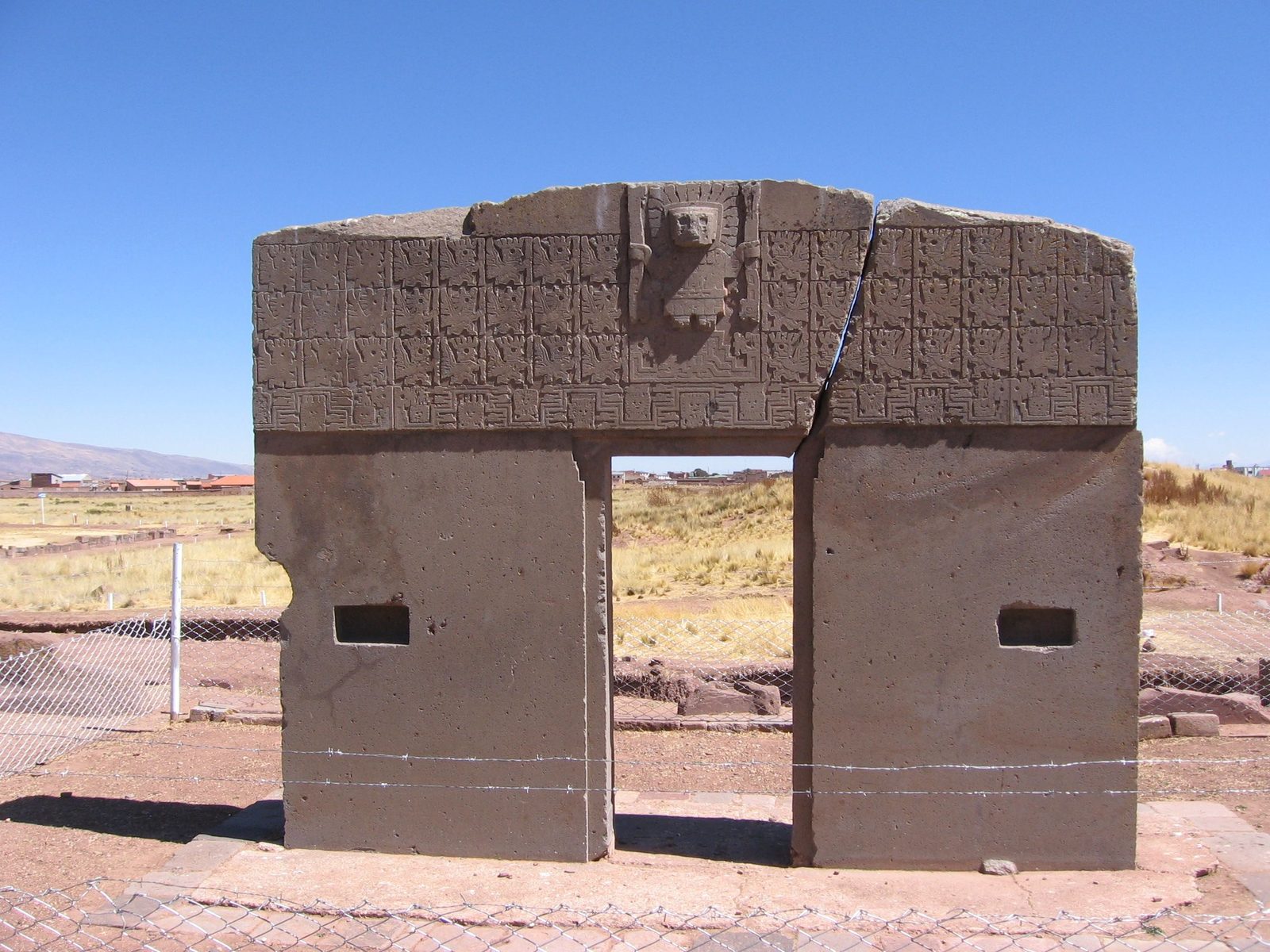 A stone gateway cut from a single block, with a carved frieze across its lintel and a crack through one side.