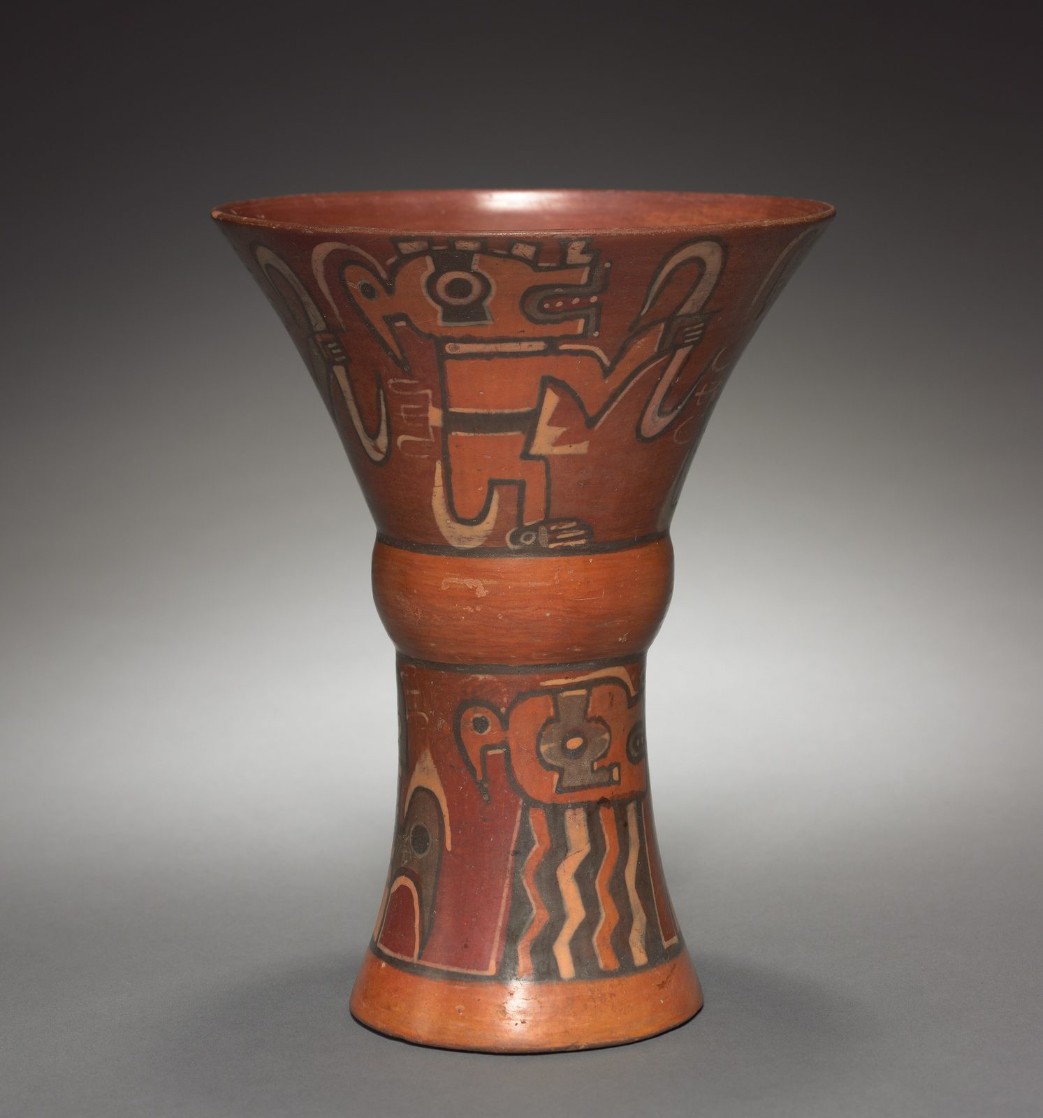 A tall flaring painted cup in red, orange and black, decorated with stylized faces.