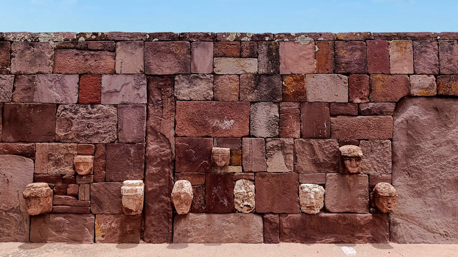 A red sandstone wall set with carved stone heads projecting at different heights.