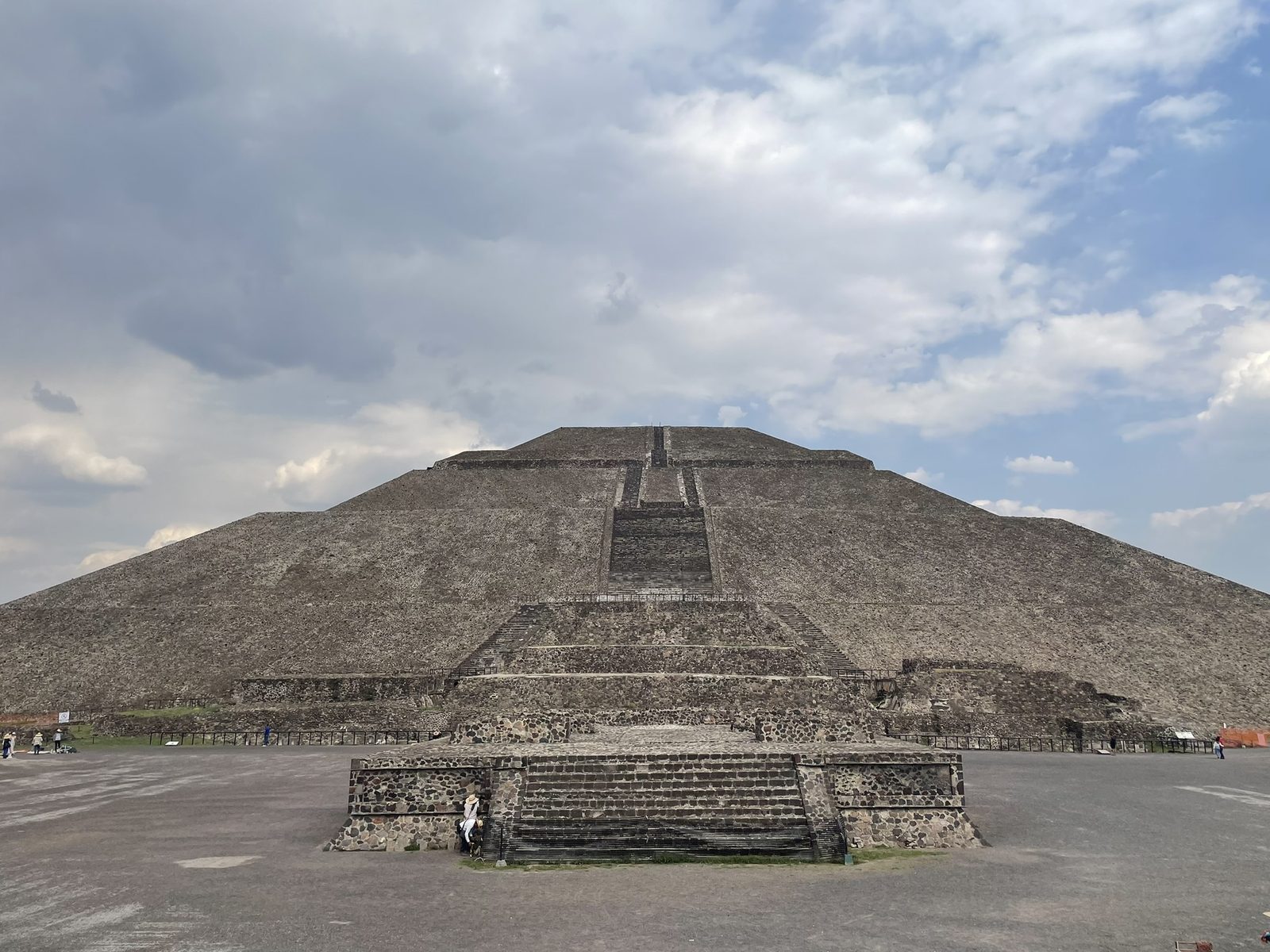 A huge stepped pyramid seen across a paved plaza under clouds.