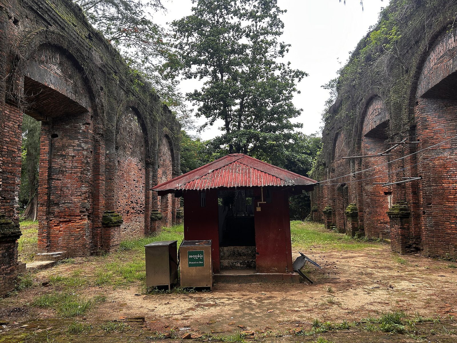 Roofless brick walls with arched openings around a small shrine.