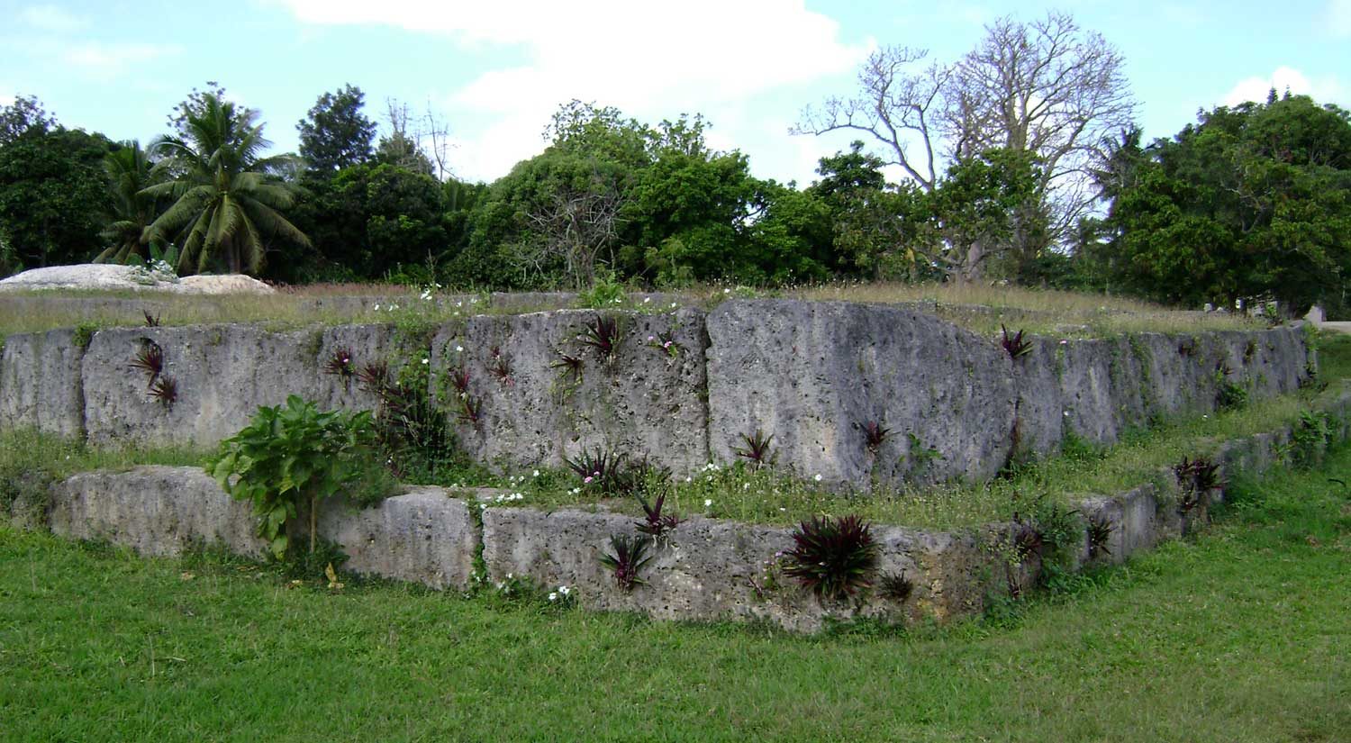 A low terraced platform faced with huge cut slabs of stone, on a lawn among trees.