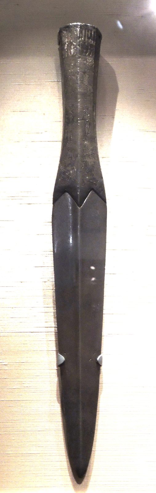 A long iron spearhead with a silver-mounted socket, in a display case.